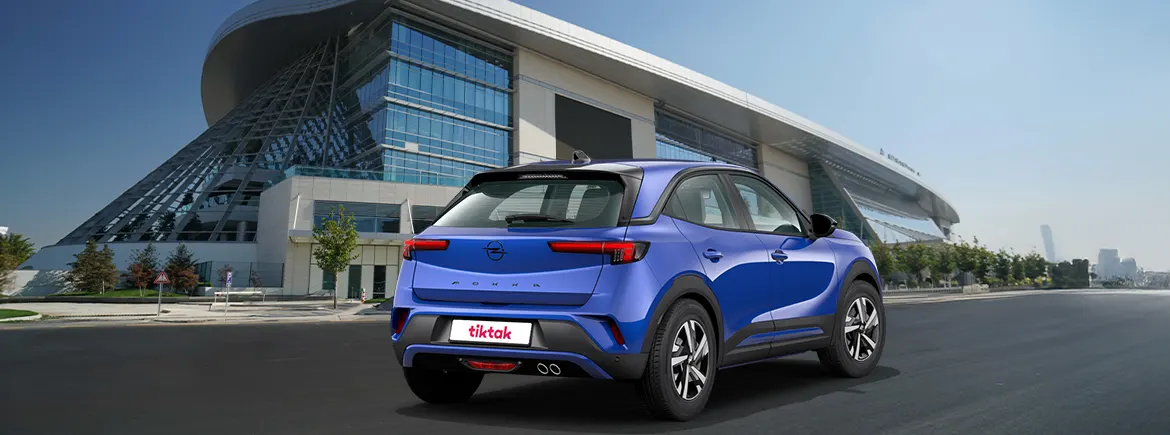 Mavi bir Opel marka SUV araba, modern bir mimari yapı önünde park halinde, şehir manzarası ile açık hava görüntüsü.