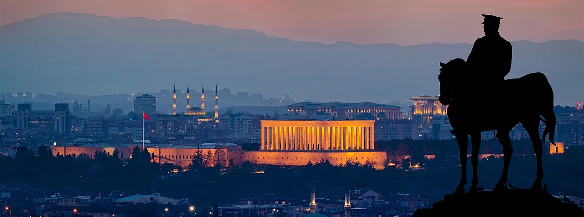 At üzerinde siluet bir Atatürk heykeli, arka planda Ankara'daki Anıtkabir ve şehir manzarası ile gün batımı atmosferi.