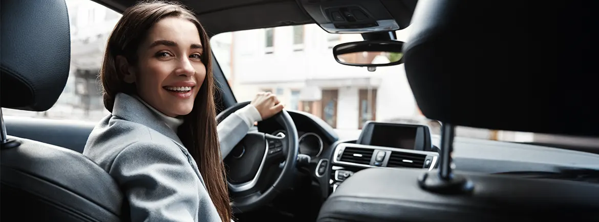 Şehir içinde araç kullanırken güler yüzlü bir kadın sürücü – tek tıkla 30 günlük araç kiralama sürecinin kolaylığı ve özgür kullanım deneyimi.