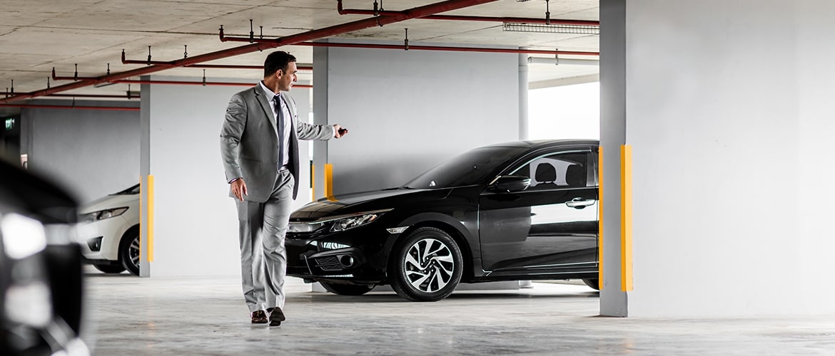 Takım elbiseli bir adam kapalı otoparkta TikTak aracıyla buluşmak üzere ilerliyor; TikTak, yoğun iş temposundaki profesyonellere hızlı ve anında araç kiralama kolaylığı sağlıyor.